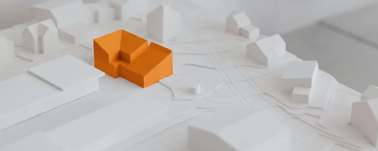A white architectural scale model of a neighbourhood, with one building picked out in orange